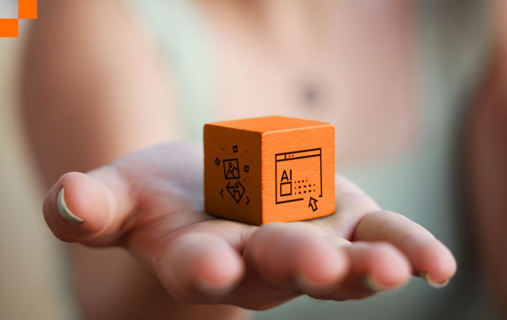 Selective focused photo of woman's hand holding an orange wooden cube with a graphic of images on one side and a graphic of Ai icon on the other