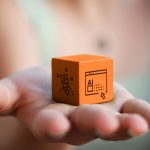 Selective focused photo of woman's hand holding an orange wooden cube with a graphic of images on one side and a graphic of Ai icon on the other
