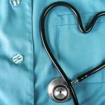 Stethoscope shaped into a heart overtop a pair of medical scrubs