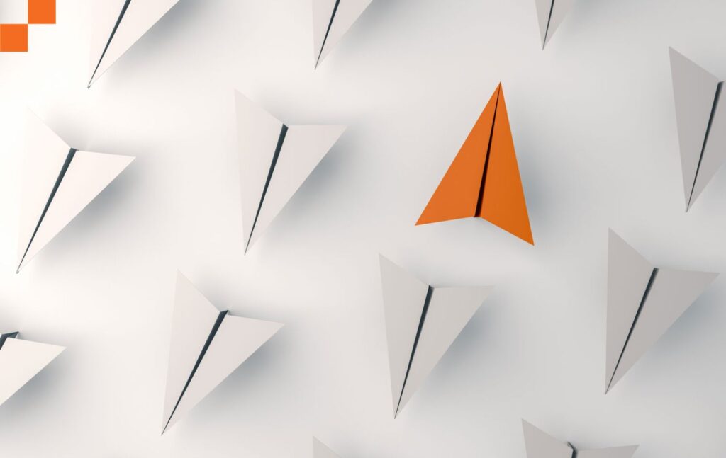 One orange paper airplane among all white paper airplanes