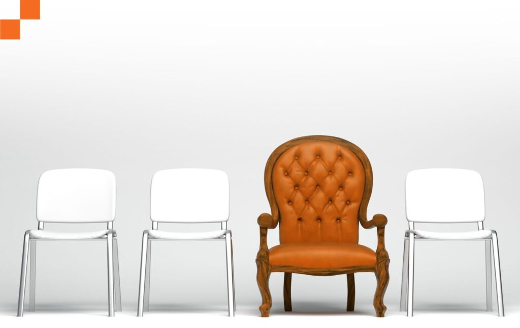 A unique apolstered orange chair placed in between plain plastic white chairs.